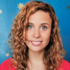 Giulia Boitani, a smiling woman with long curly brown hair wearing a red jumper against a bright blue background