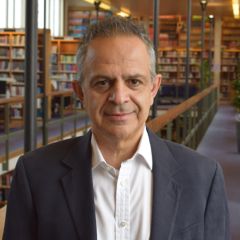 Hamid Sabourian, a smiling man with short grey hair wearing a white shirt and a navy blue jacket. He is in a Library.