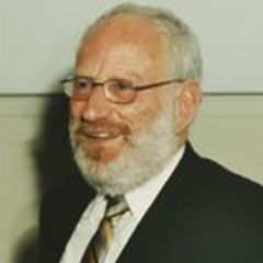 Herbert Huppert, a smiling man with short grey hair, a beard and glasses wearing a dark suits and tie