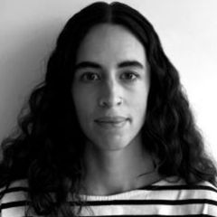 Jane Hall, a black and white image of a smiling woman with long dark, wavy hair and a nose ring wearing a striped top.