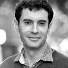 Jason Sharman, a black and white image of a smiling man with short dark hair. He is wearing a shirt and a sweater.
