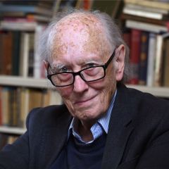 John Dunn, a smiling bald man with rectangular glasses and a black blazer in front of book shelves