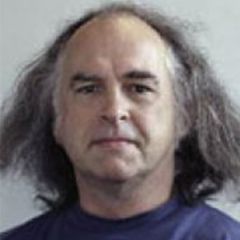 John Henderson, a smiling man with shoulder length grey hair wearing a blue t-shirt