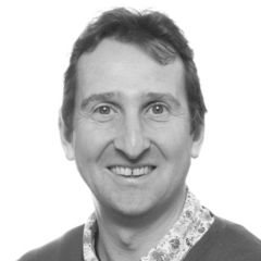 Julian Griffin, a black and white image of a smiling man with short dark hair wearing a floral shirt and a jumper