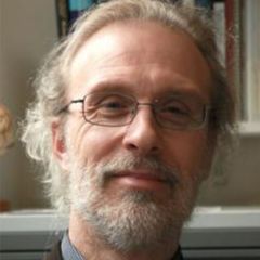 Mark Johnson, a smiling man wearing glasses with grey hair, beard and glasses. He is sitting in front of a bookshelf.