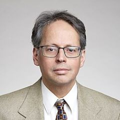 Mark Gross, a smiling man with grey hair wearing glasses and a beige suit