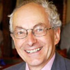 Martin Hyland, a smiling man with short grey hair and glasses. He is wearing a pink shirt and a grey jacket.