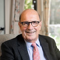 Michael Proctor, a bald smiling man with glasses wearing a black jacket, a pale blue shirt and a pink tie 