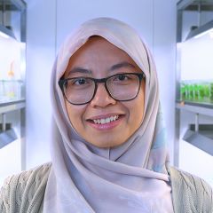 Nadia Mohd-Radsman, a smiling woman wearing a white headscarf and black glasses. She is standing in a lab