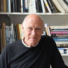 Nick Bullock, a smiling bald man wearing a grey jumper and standing in front book shelves