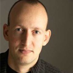 Richard Causton, a man with short dark hair and a grey jumper against a dark grey background