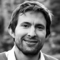 Sebastian Ahnert, a black and white photo of smiling man with mid length dark hair, stubble a shirt and a jumper