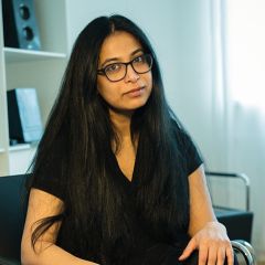 Surabhi Ranganathan, a smiling woman with long black hair and and glasses wearing a black top. She is sitting in a light office.