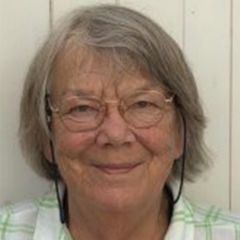 Tess Adkins, a smiling woman with shaort grey hair and glasses wearing a green and white checked shirt