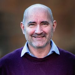 Timothy Flack, a smiling bald man wearing a purple sweater