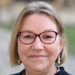 A white woman with blonde hair and red-framed glasses