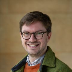 A white man with brown hair and brown-framed glasses