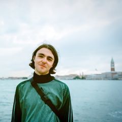 A man in a green top in front of a Venetian lagoon