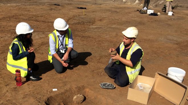 Archaelogists at the Croft Gardens site, wearing hard hats and hi vis vests, one holding an Anglo Saxon pot