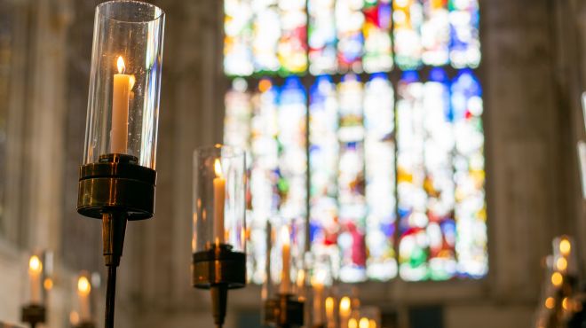 Candles lit with stained glass window in the background