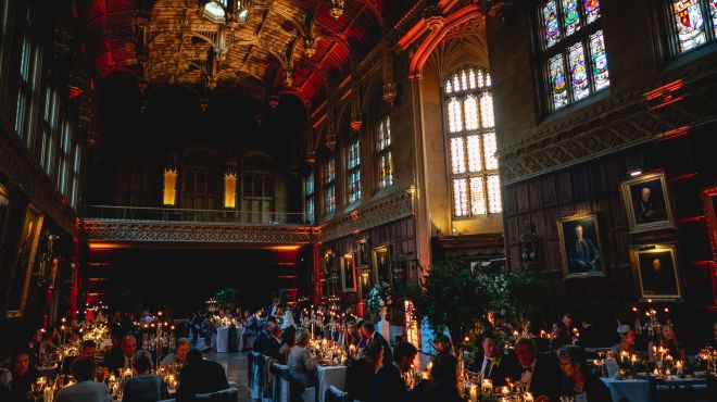 Wedding guests seated at dinner in a formal hall with stained glass windows