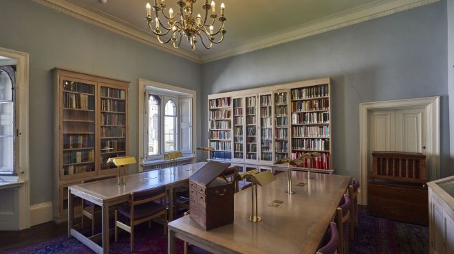 a reading room with tables chairs and bookcases lit by a chandelier