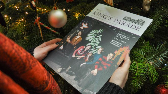 Hands holding a copy of King's Parade next to a Christmas tree
