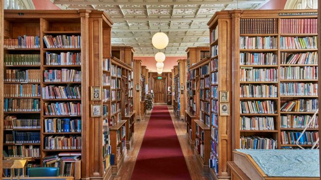 A library with oak bookshelves, a red carpet and round lights