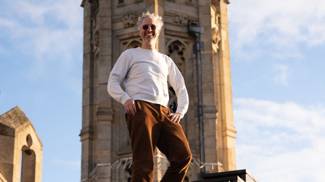 A white man wearing sunglasses with a tower and blue sky in the background