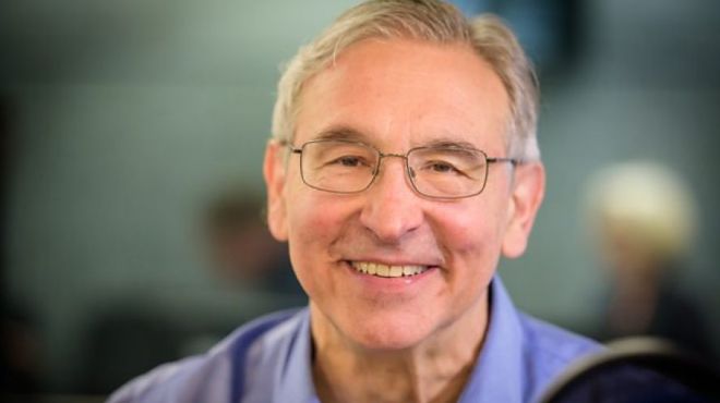 A white man with glasses and short grey hair wearing a light blue shirt