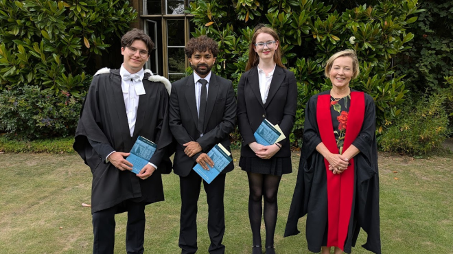 Three students holding books with the Provost, all wearing academic dress in a garden