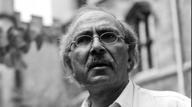 A black and white photo of a man with glasses wearing light coloured clothing