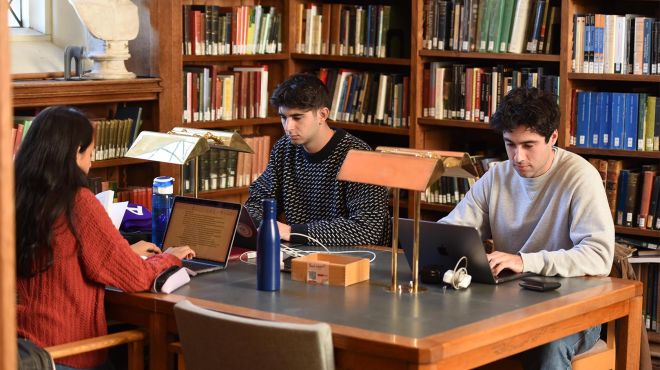 Three students working on their laptops at a table in the Library 