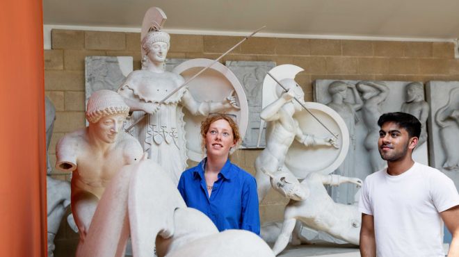 Two students look at reproductions of classical marble sculptures in a museum