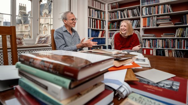 A student and supervisor sitting behind a pile of books