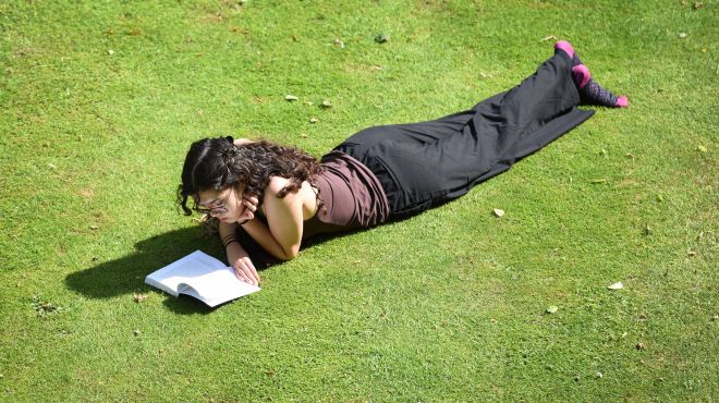 female student lying on lawn reading