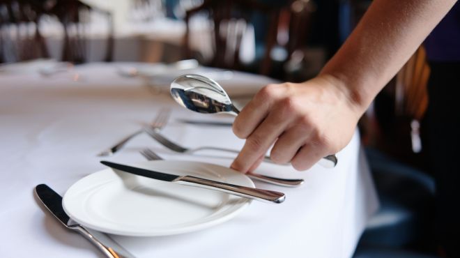 A person laying a place setting at a table