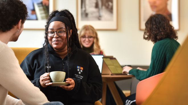 Two students sat in the bar drinking coffee with two students on their laptops in the background