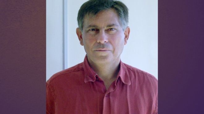 A smiling man with dark grey hair and a red shirt