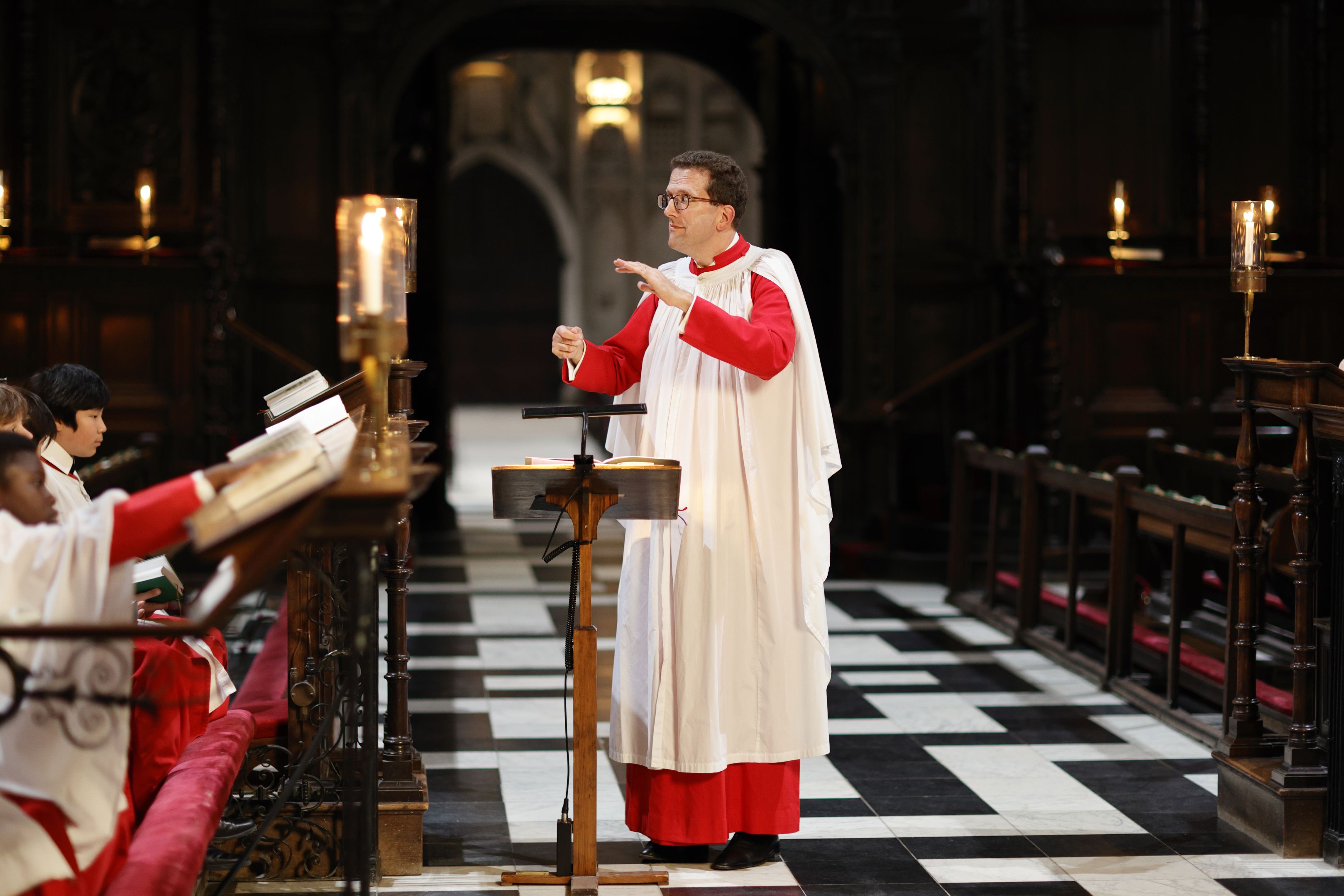 A man wearing red and white robes conducting a choir