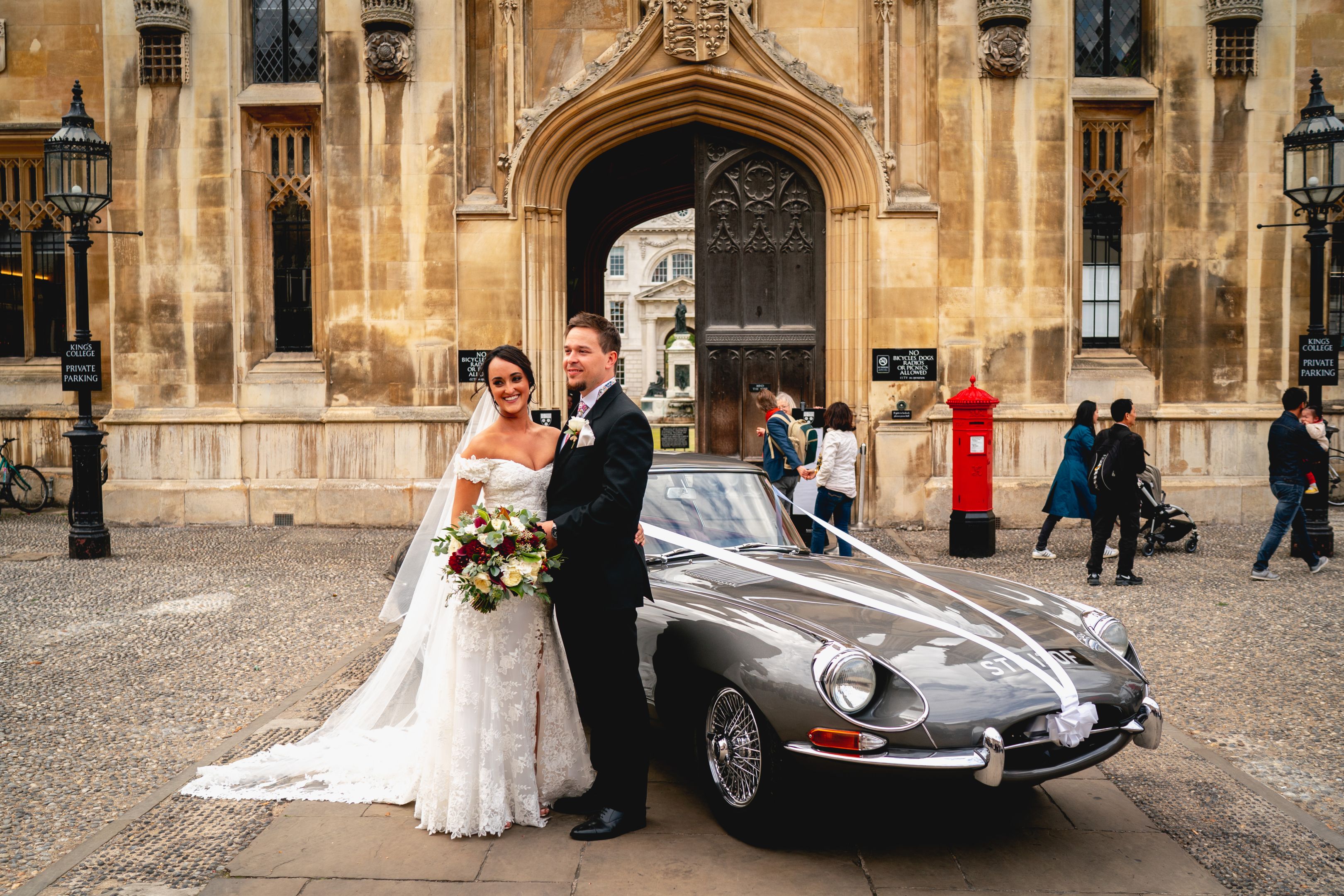 A bride and groom in front of a classic car and gothic archway