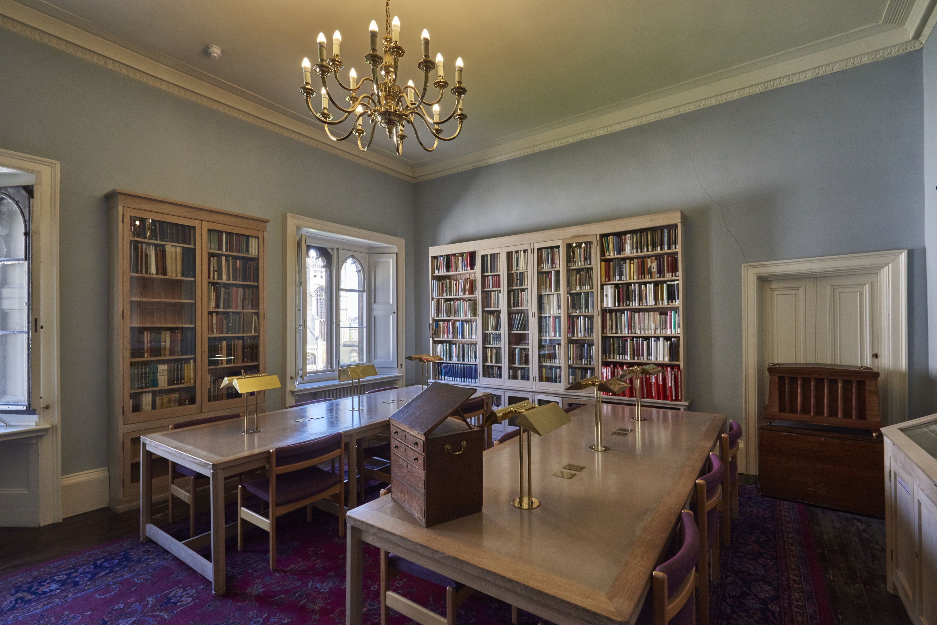 a reading room with tables chairs and bookcases lit by a chandelier