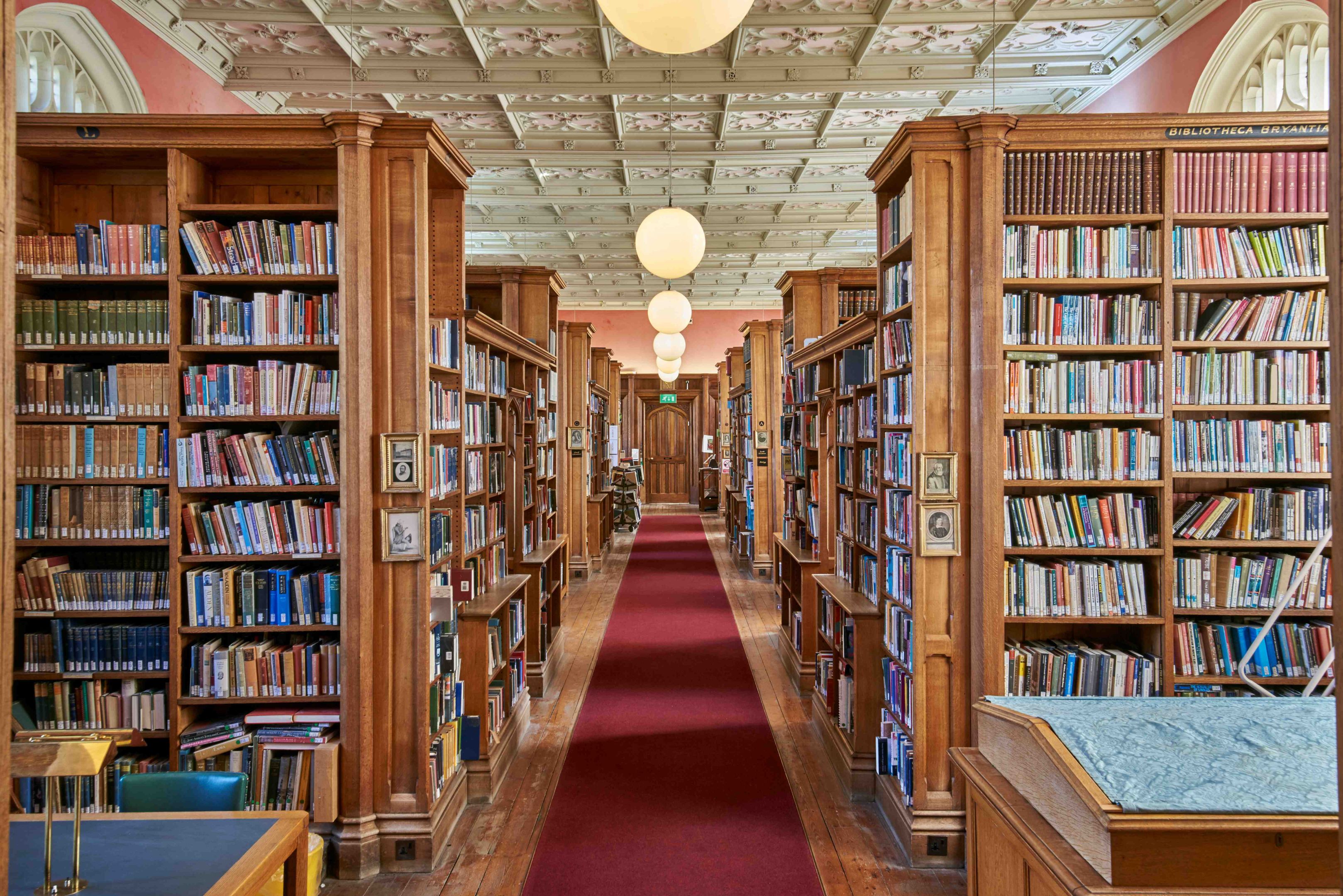 A library with oak bookshelves, a red carpet and round lights