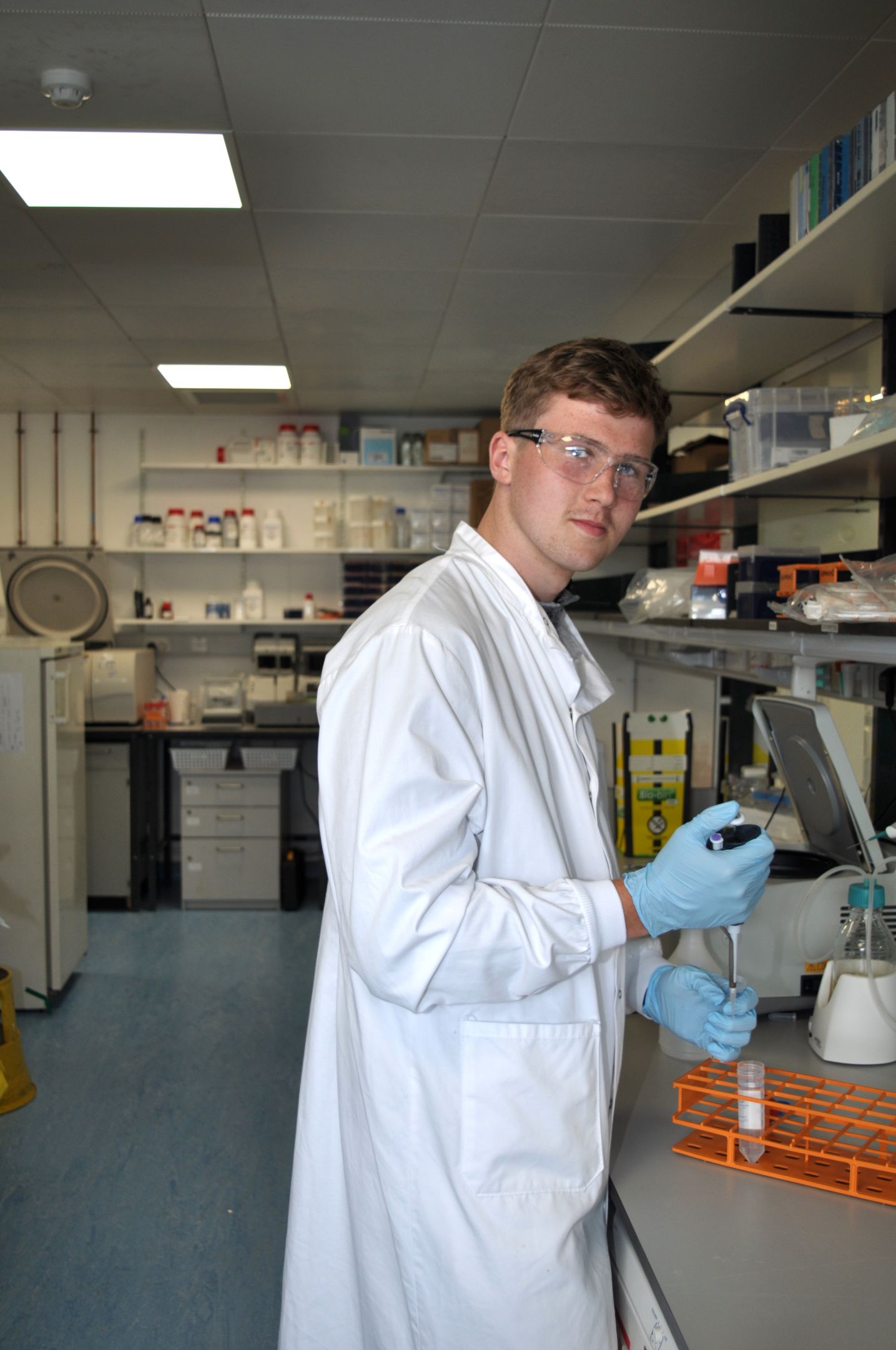 Male student wearing lab coat and goggles in a lab