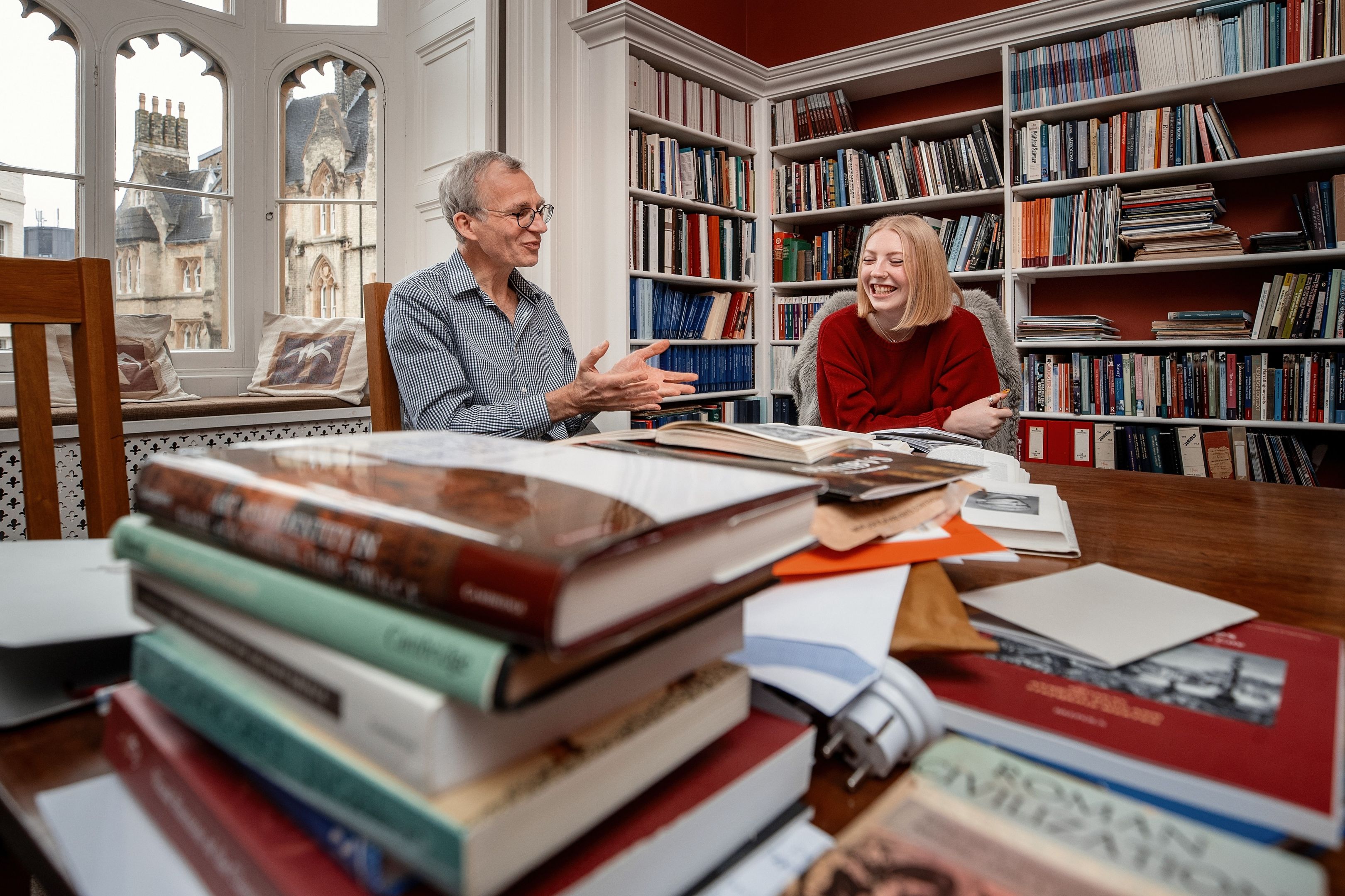 a male professor and a female student with a stack of books in foreground