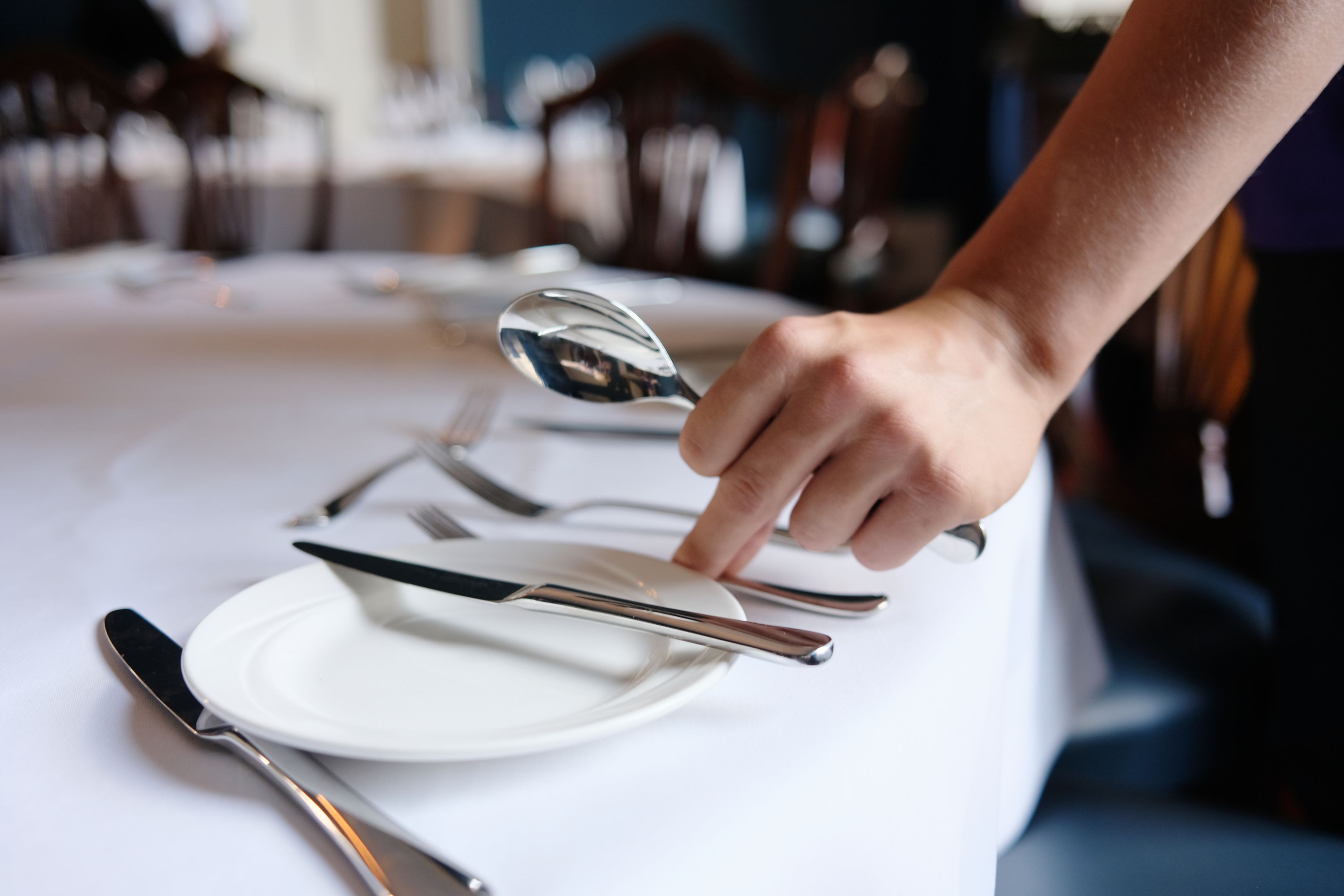 A person laying a place setting at a table