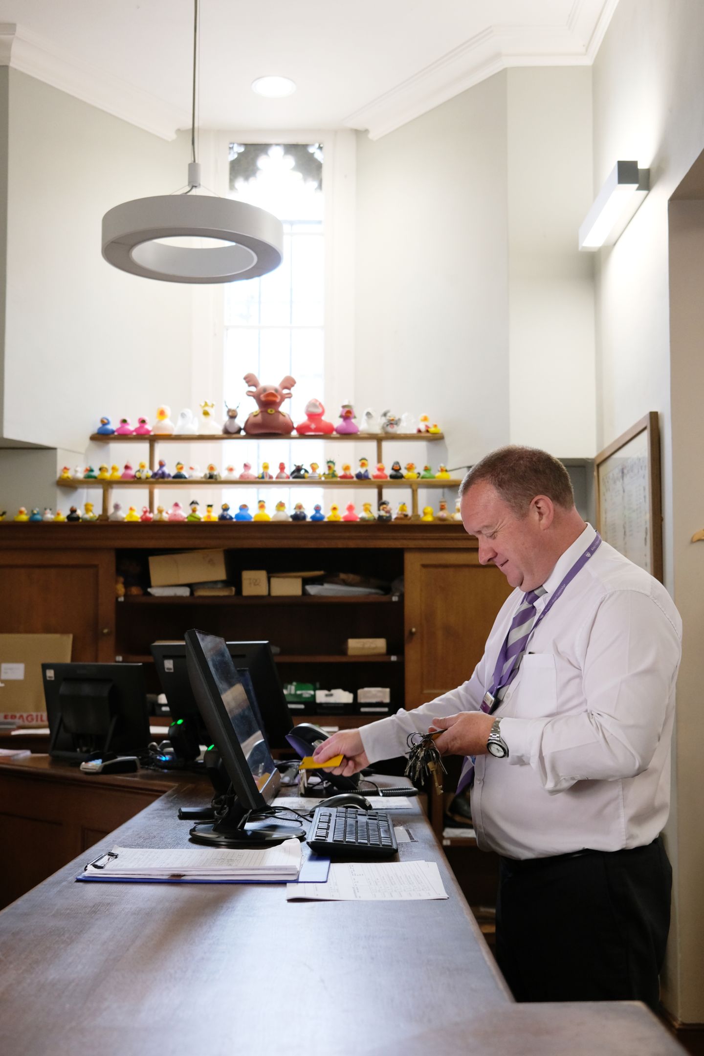 A man standing in front of a computer screen with shelves of rubber ducks in the background